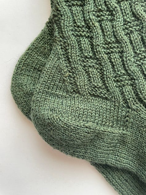 A green hand knit sock with a basket weave pattern.