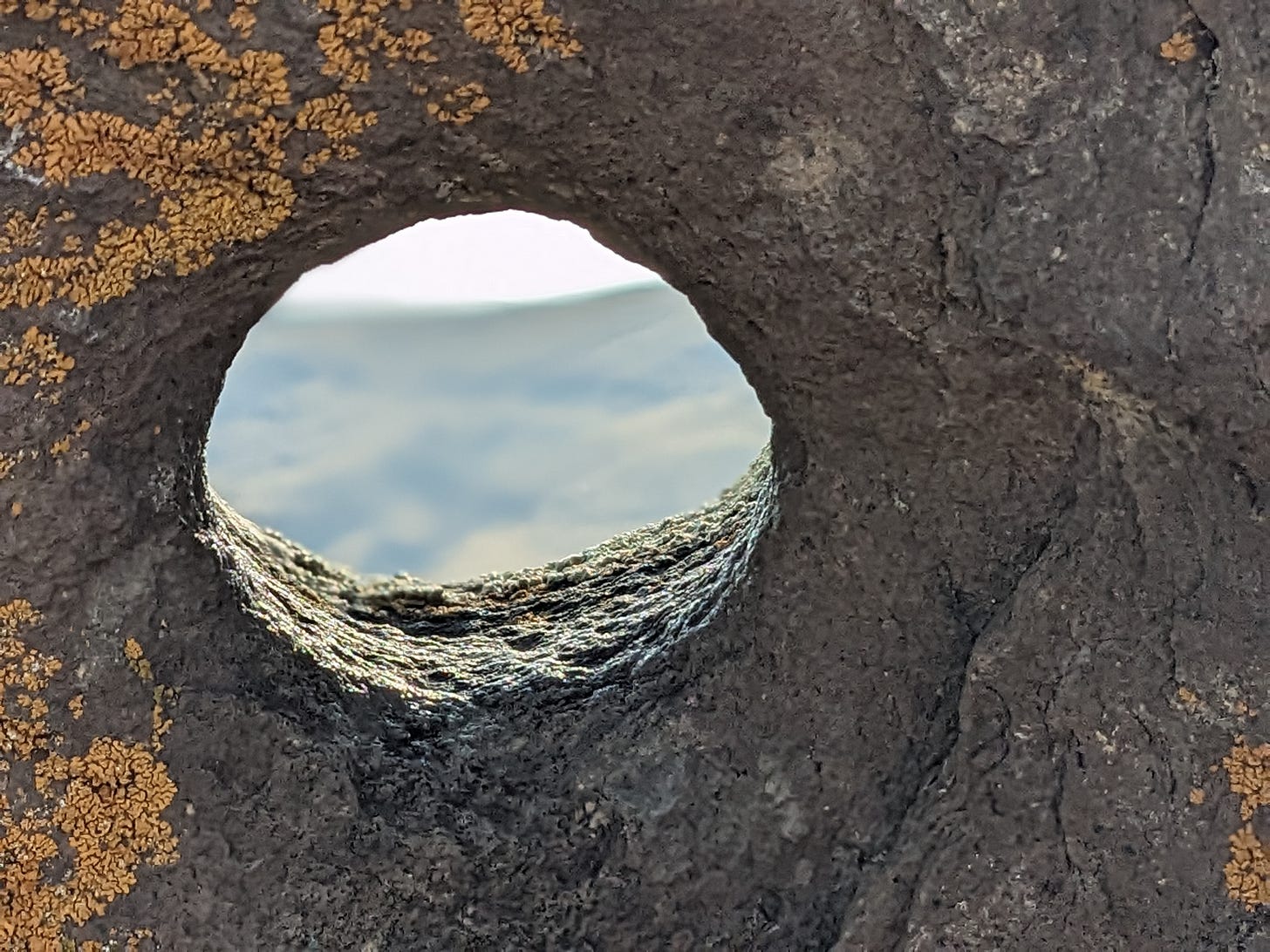 A grey speckled rock with a perfect circle carved, through which you can see the gold mountainside beyond.   