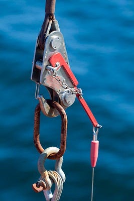 A quick release connects two cables with a rusty link, with water in the background. 