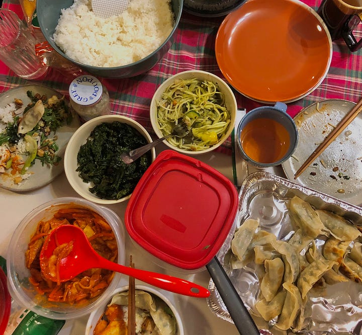 On the left is an ancestral shrine with white and yellow flowers, a framed photo of Jenn's dog Coco, a tube of incense stickers, clementines, a tray of gold chocolate coins and rice crackers. On the right is a tablespread of food, including dumplings, tteokbokki, rice and salad.