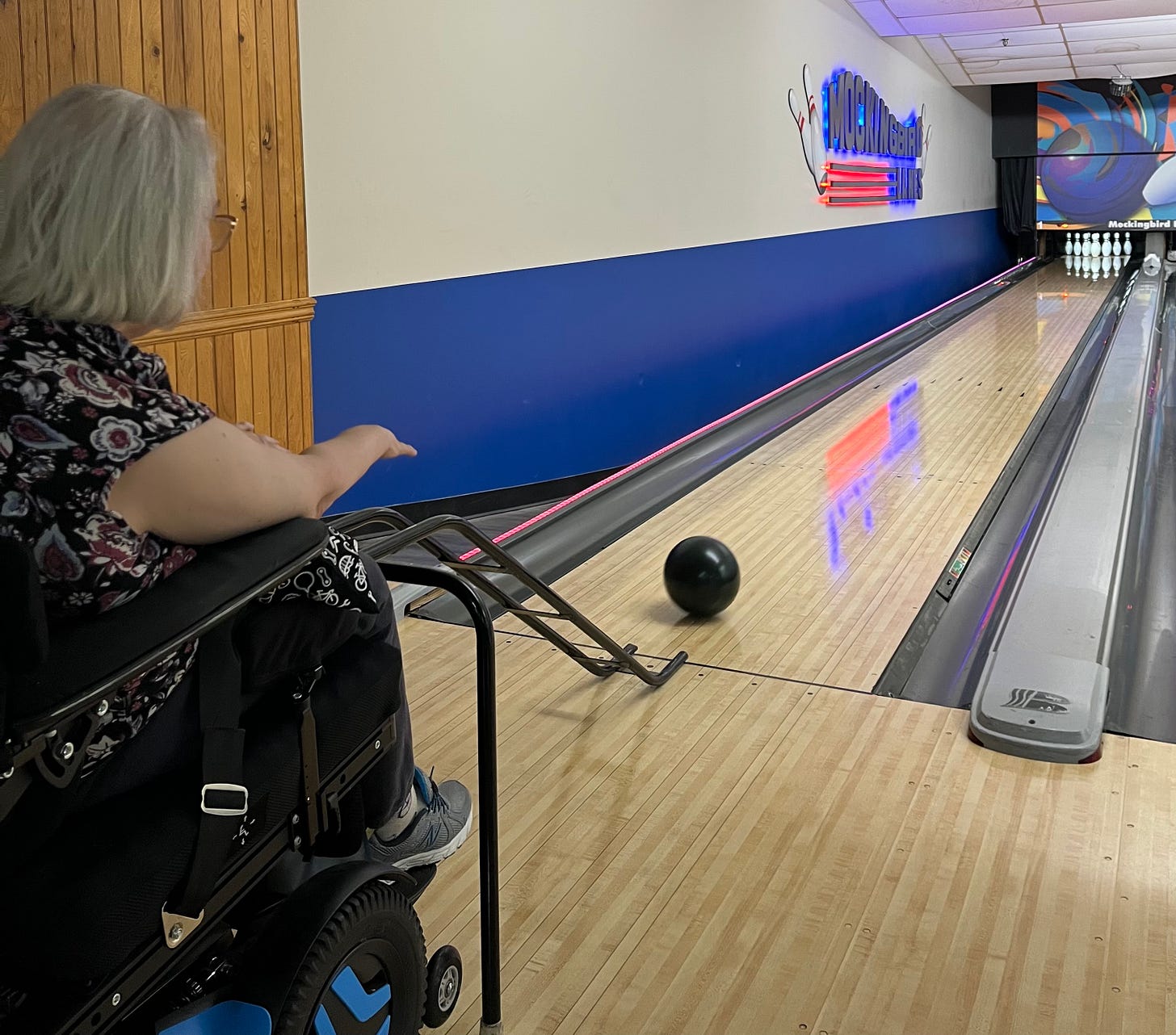 Debbie in her wheelchair pushing a bowling ball down a ramp at a bowling alley