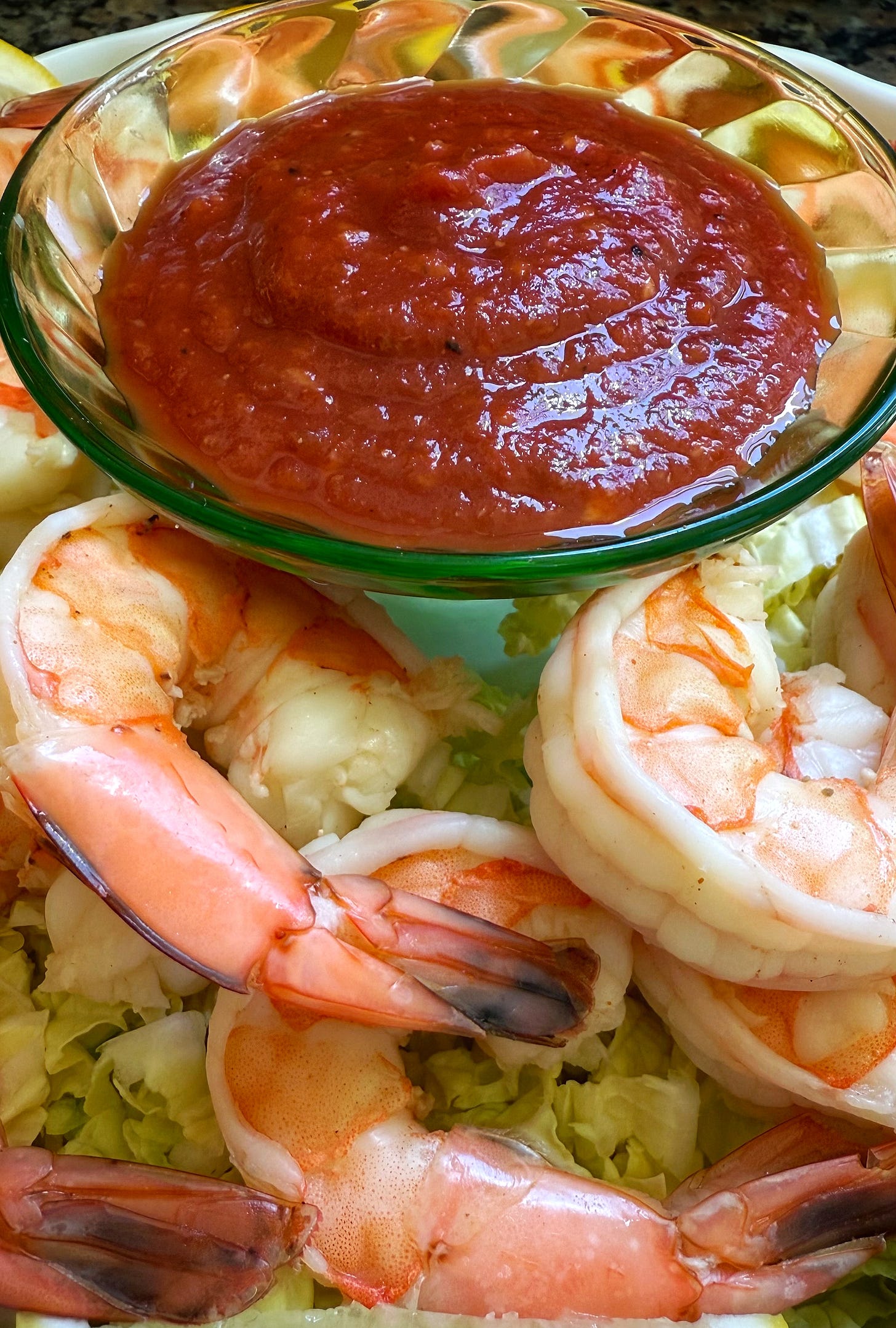 A green Depression glass bowl of cocktail sauce surrounded by poached and peeled shrimp.