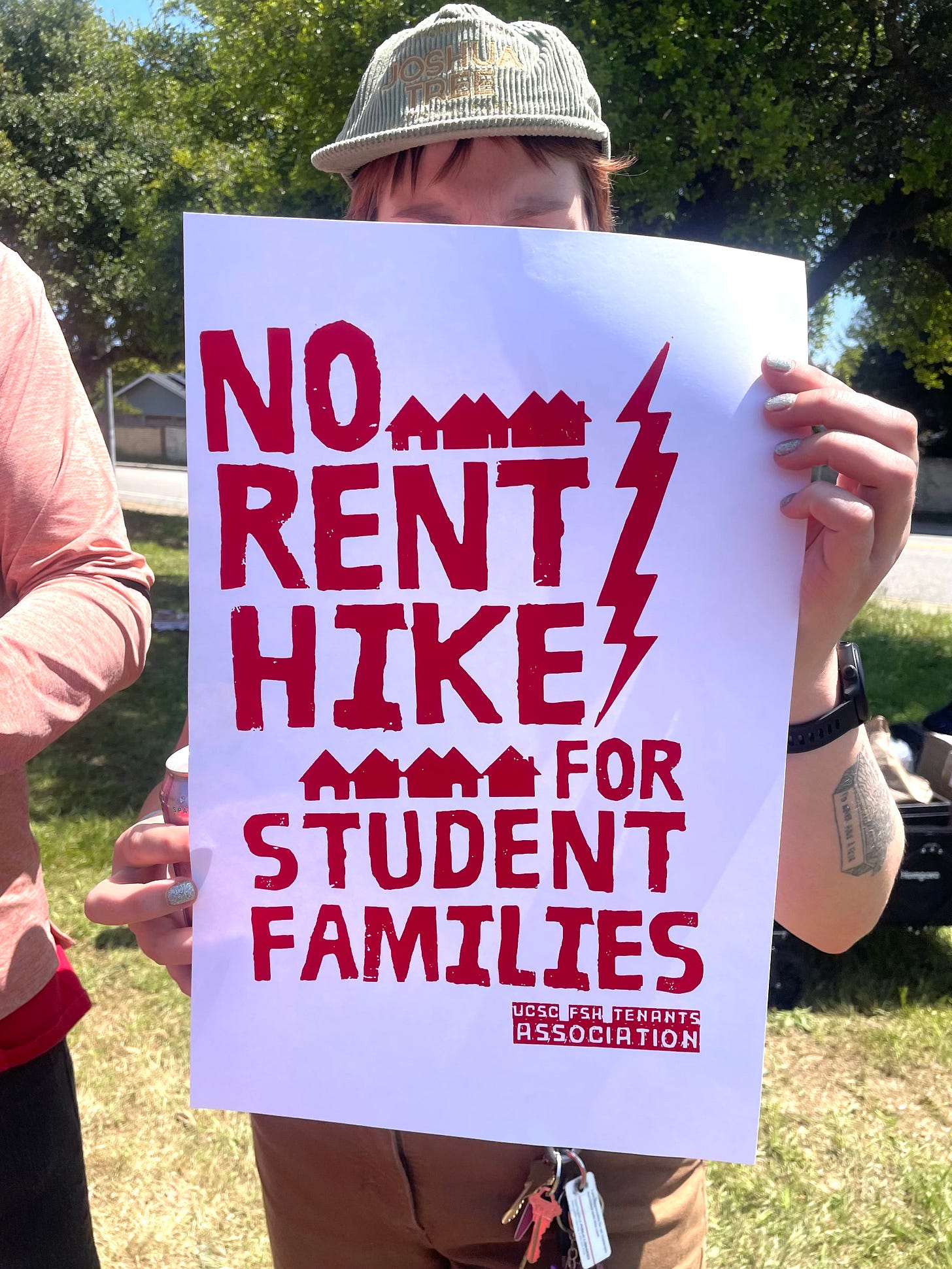 person in cap with sign: "No rent hikes for student families" person in cap with sign: "No rent hikes for student families"