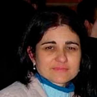 mulher de cabelos longos e escuros sorri levemente e usa uma blusa de cor clara mulher de cabelos longos e escuros sorri levemente e usa uma blusa de cor clara