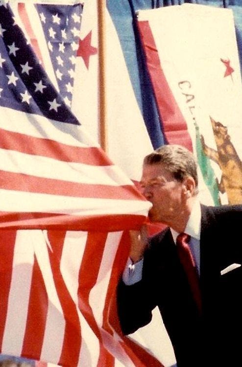 This may contain: a man in a suit and tie holding an american flag with other flags behind him