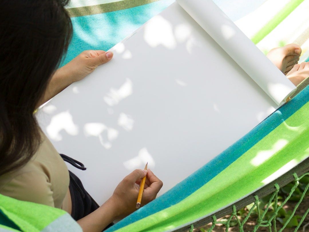a woman sitting in a hammock writing on a piece of paper