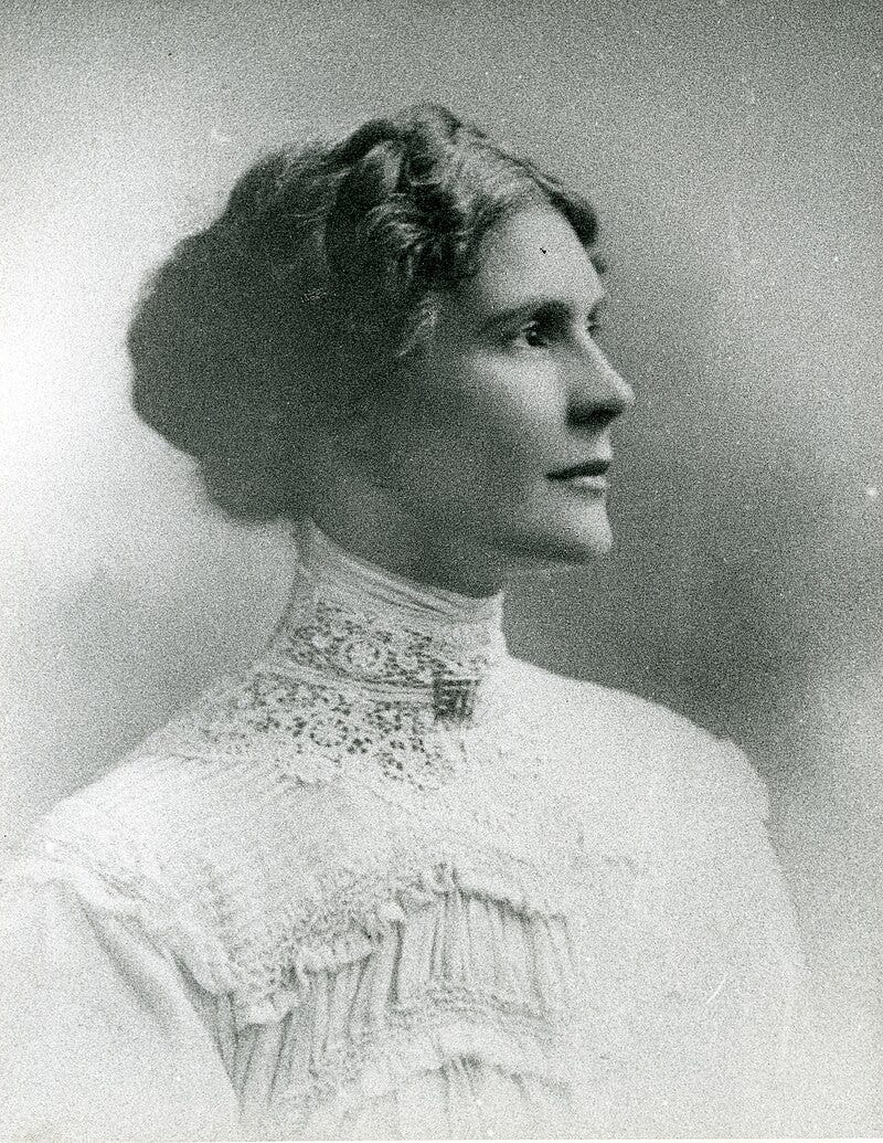 A sepia-toned portrait of a woman with wavy hair styled in an updo, wearing a high-collared lace blouse, gazing to the right with a serene expression.