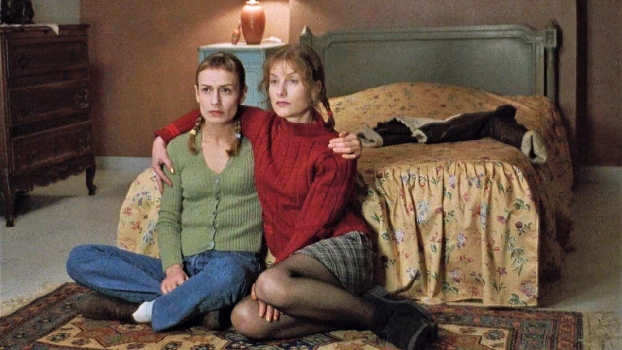 Sandrine Bonnaire and Isabelle Huppert as Sophie and Jeanne, two young white women, sitting on the floor of a bedroom, watching TV, their arms around each other Sandrine Bonnaire and Isabelle Huppert as Sophie and Jeanne, two young white women, sitting on the floor of a bedroom, watching TV, their arms around each other