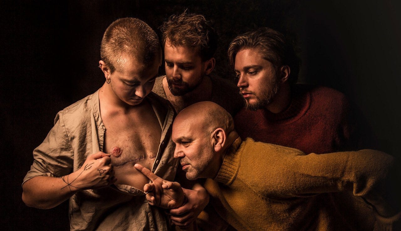 Photograph of four figures staged to imitate Caravaggio's famous painting of Thomas touching Christ's side wound. In this version, the person playing Jesus has top surgery scars, which his three friends marvel at. He is guiding the hand of one friend so that the friend's pointer finger rests just under the scar. Photograph of four figures staged to imitate Caravaggio's famous painting of Thomas touching Christ's side wound. In this version, the person playing Jesus has top surgery scars, which his three friends marvel at. He is guiding the hand of one friend so that the friend's pointer finger rests just under the scar.