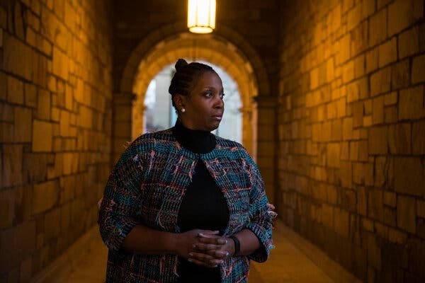 Lisa Cook, wearing a multicolor jacket over a dark top, stands in a stone corridor.