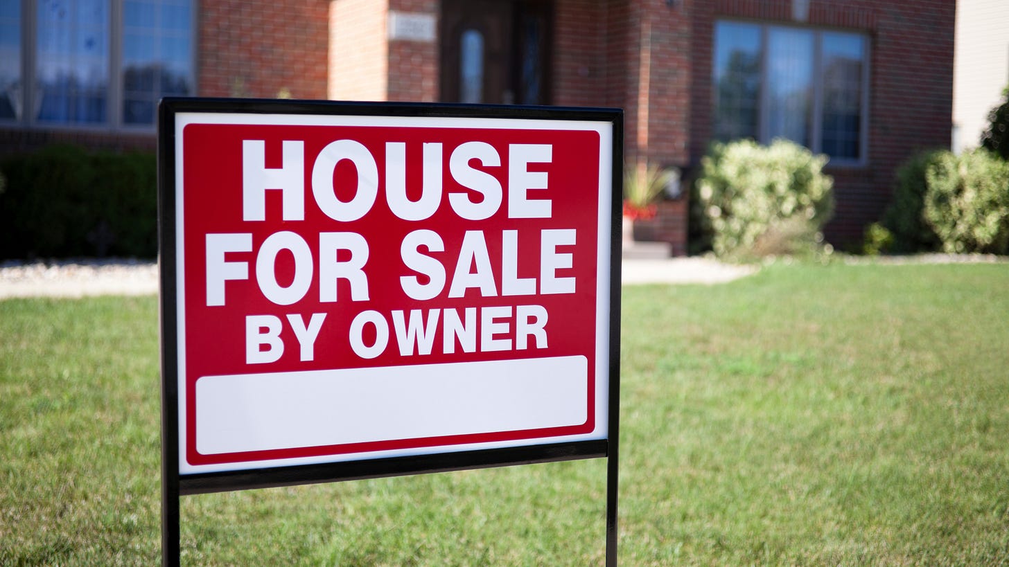A red and white For Sale By Owner sign staked in a front lawn, with a brick house behind it A red and white For Sale By Owner sign staked in a front lawn, with a brick house behind it