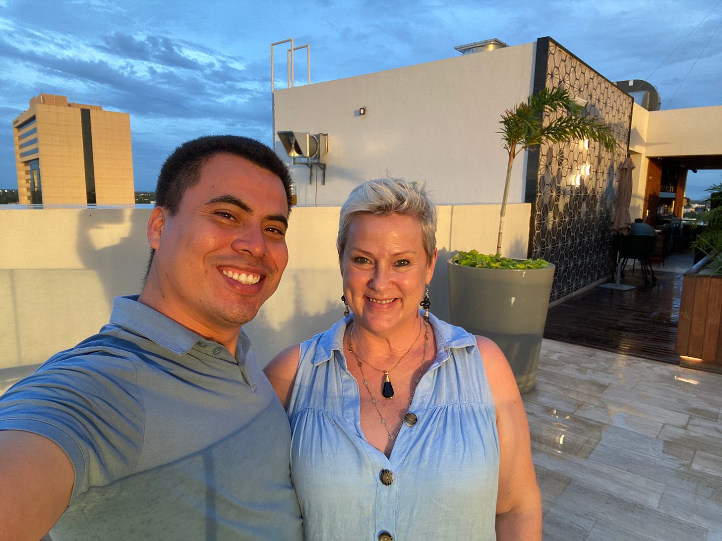 Angel Rodriguez and Amy Jones of Life in Mérida at the rooftop lounge of the Marriott Courtyard in Centro with the Hyatt Hotel in the background at sunset