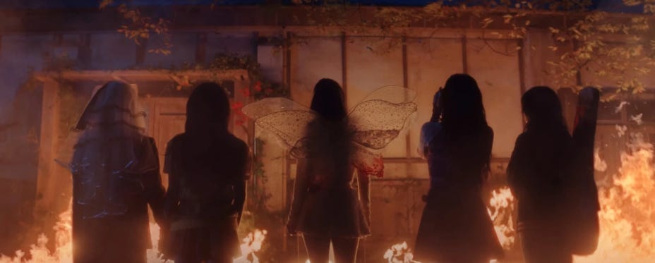 Red Velvet standing before a burning home. Left to right: Yeri, Wendy, Irene, Joy, Seulgi.