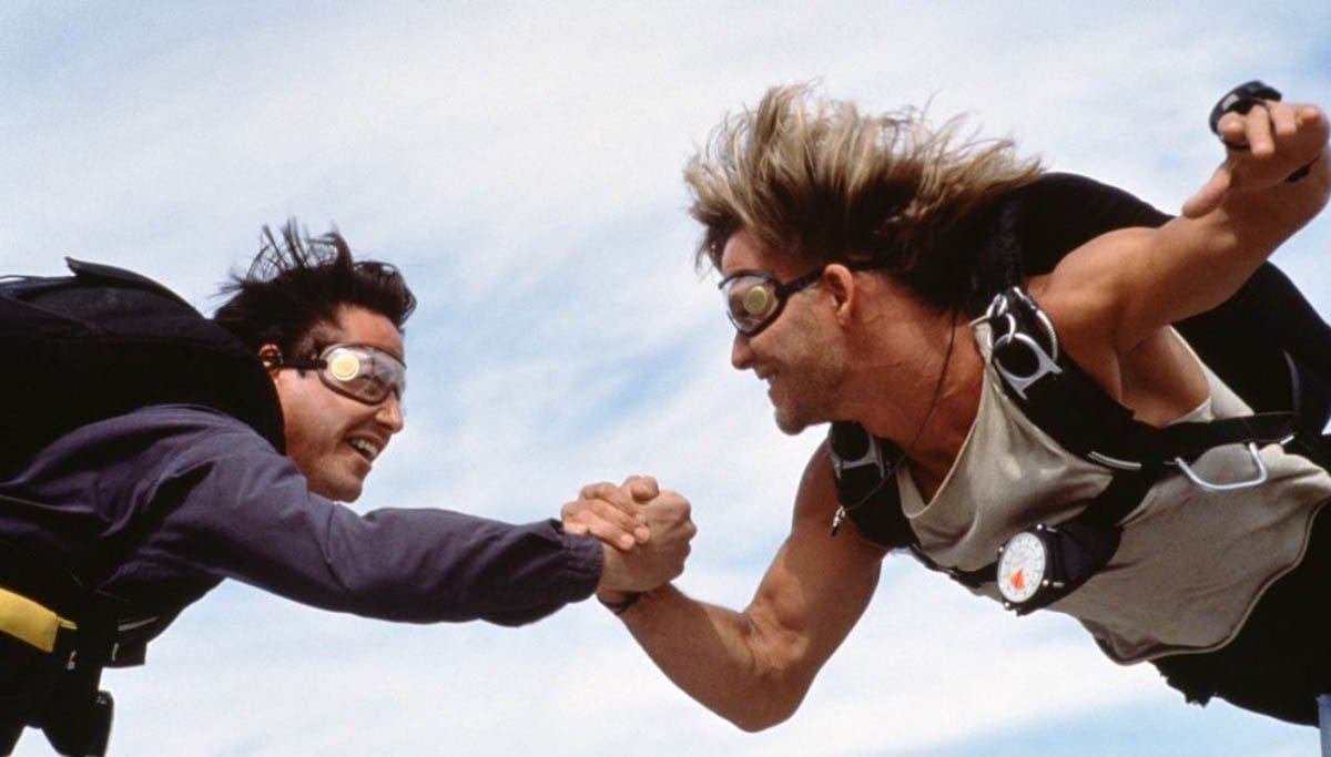 A still from Kathryn Bigelow’s 1991 surf thriller, Point Break. Keanu Reeves and Patrick Swayze grip each other’s hands mid-skydive.
