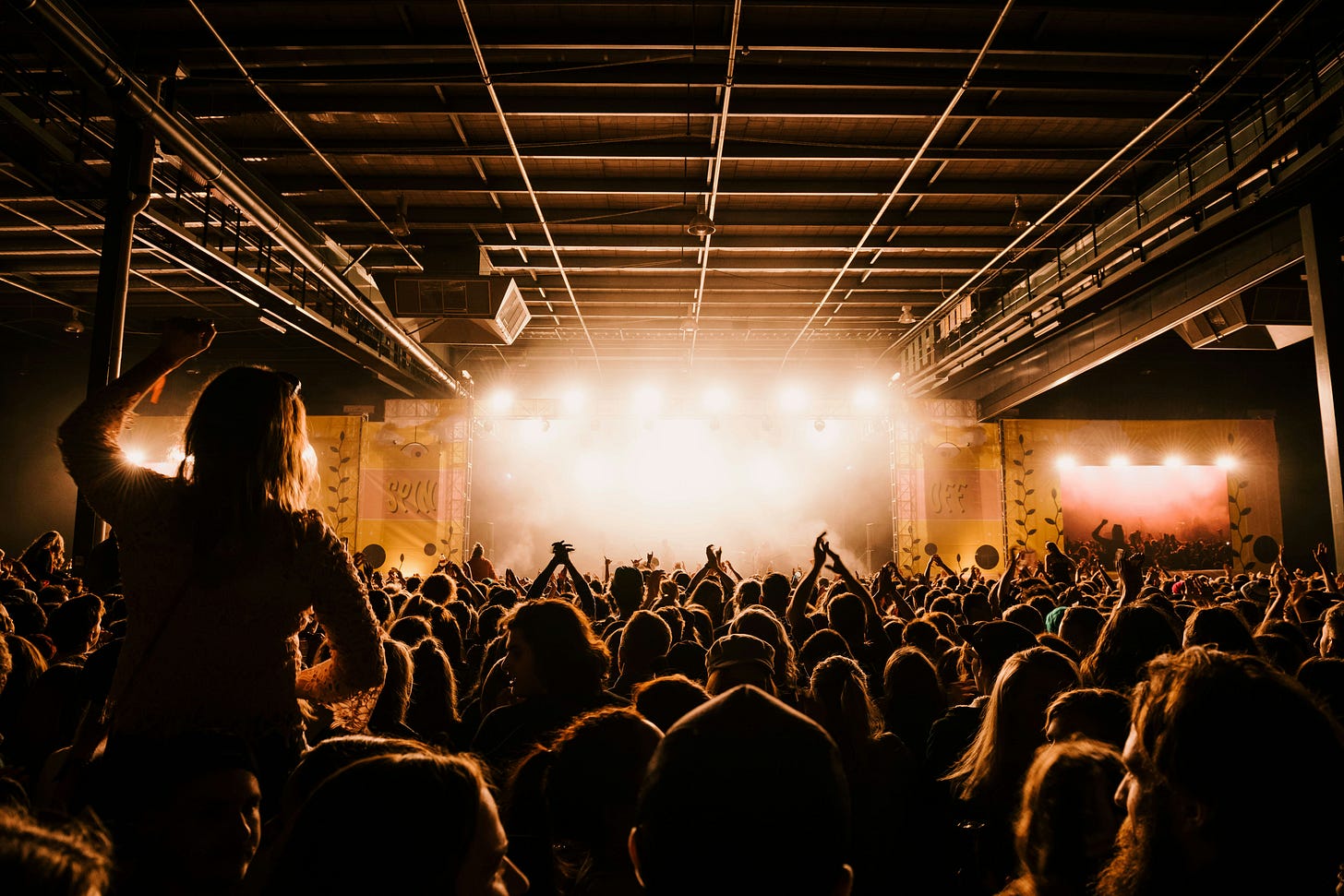 A crowd of people stands in front of a lit up stage. 