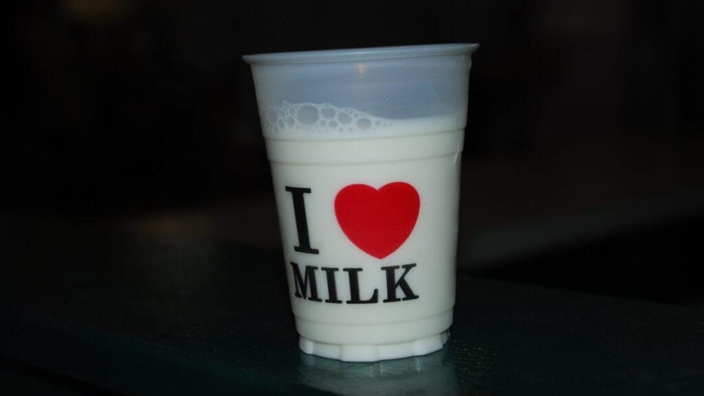 A plastic cup of milk with a design that reads “I [image of a red heart] MILK”