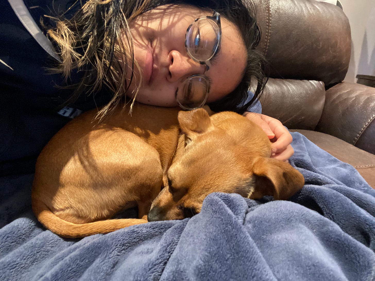 A selfie of Joelle resting her cheek on her sister's Chihuaha-Daschund mix curled up on a blanket