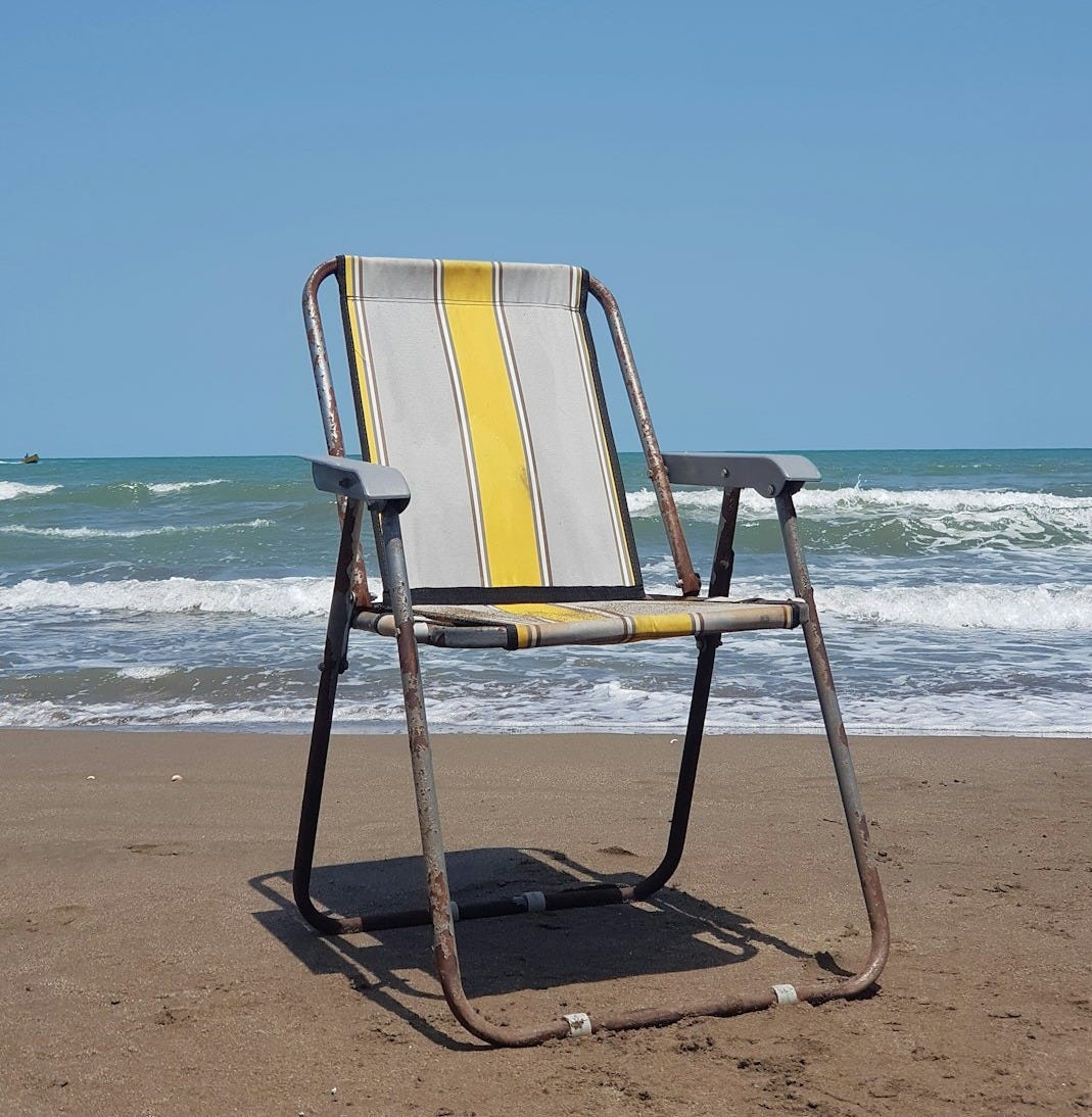 a chair sitting on a beach next to the ocean a chair sitting on a beach next to the ocean