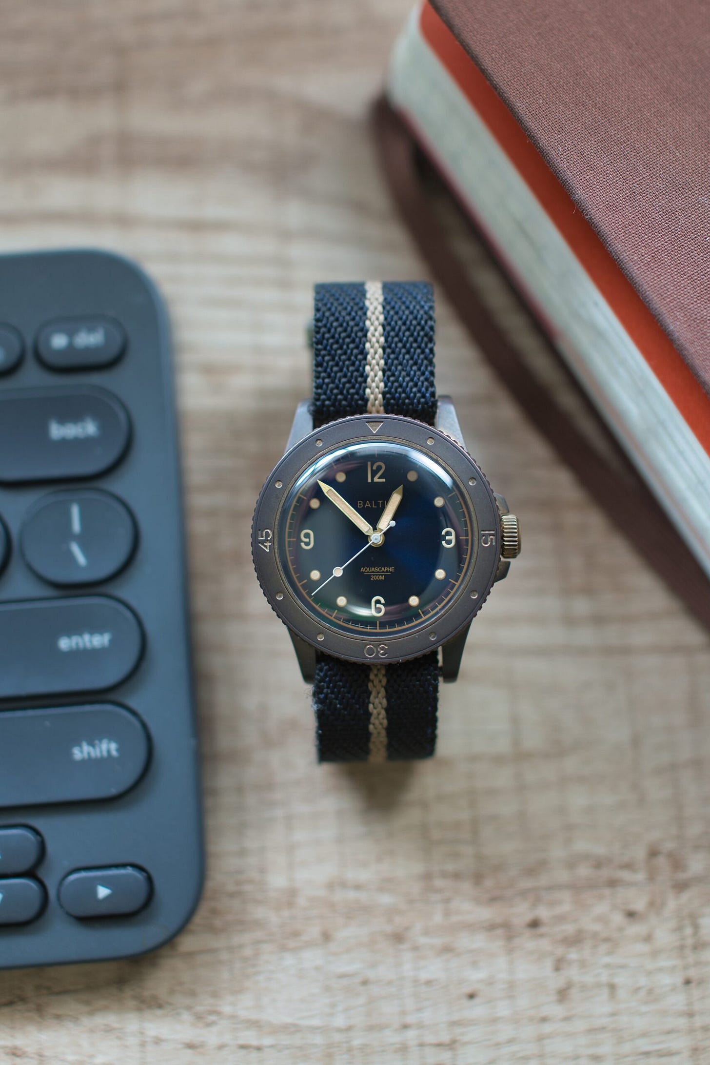 Aquascaphe Bronze on Blue/Harvest stripe Crown and Buckle Chevron Strap on wooden desk next to computer keyboard and brown Molskine journal