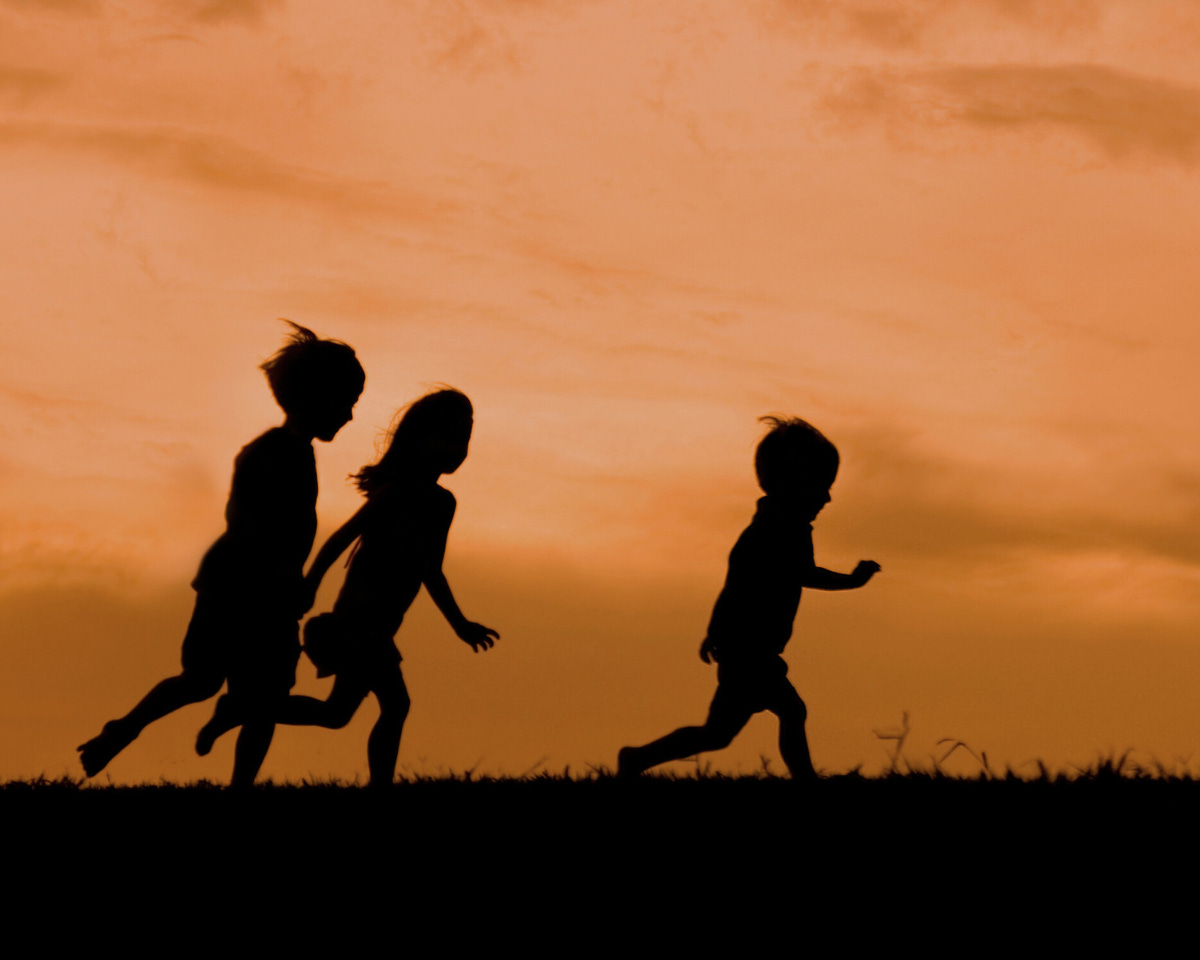 Tre bambini che corrono al tramonto in un prato, immagine simbolica che rappresenta la “Famiglia del Bosco”: natura, libertà e infanzia semplice, lontana dagli schemi della società.