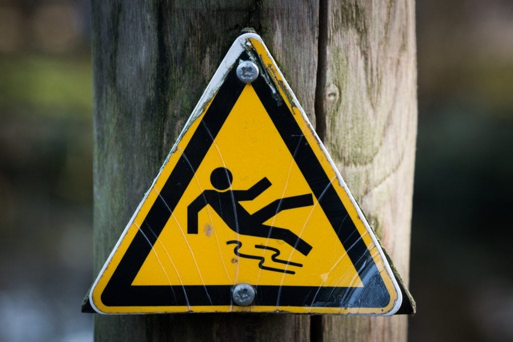 Caution sign with black stick figure outline of person falling on slippery walkway like writing in a storm