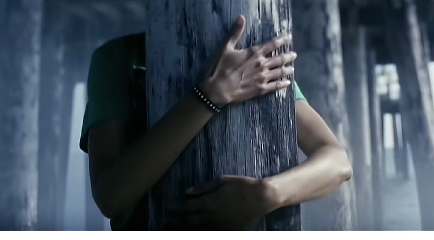 a girl's arms wrapped around a timber of a pier