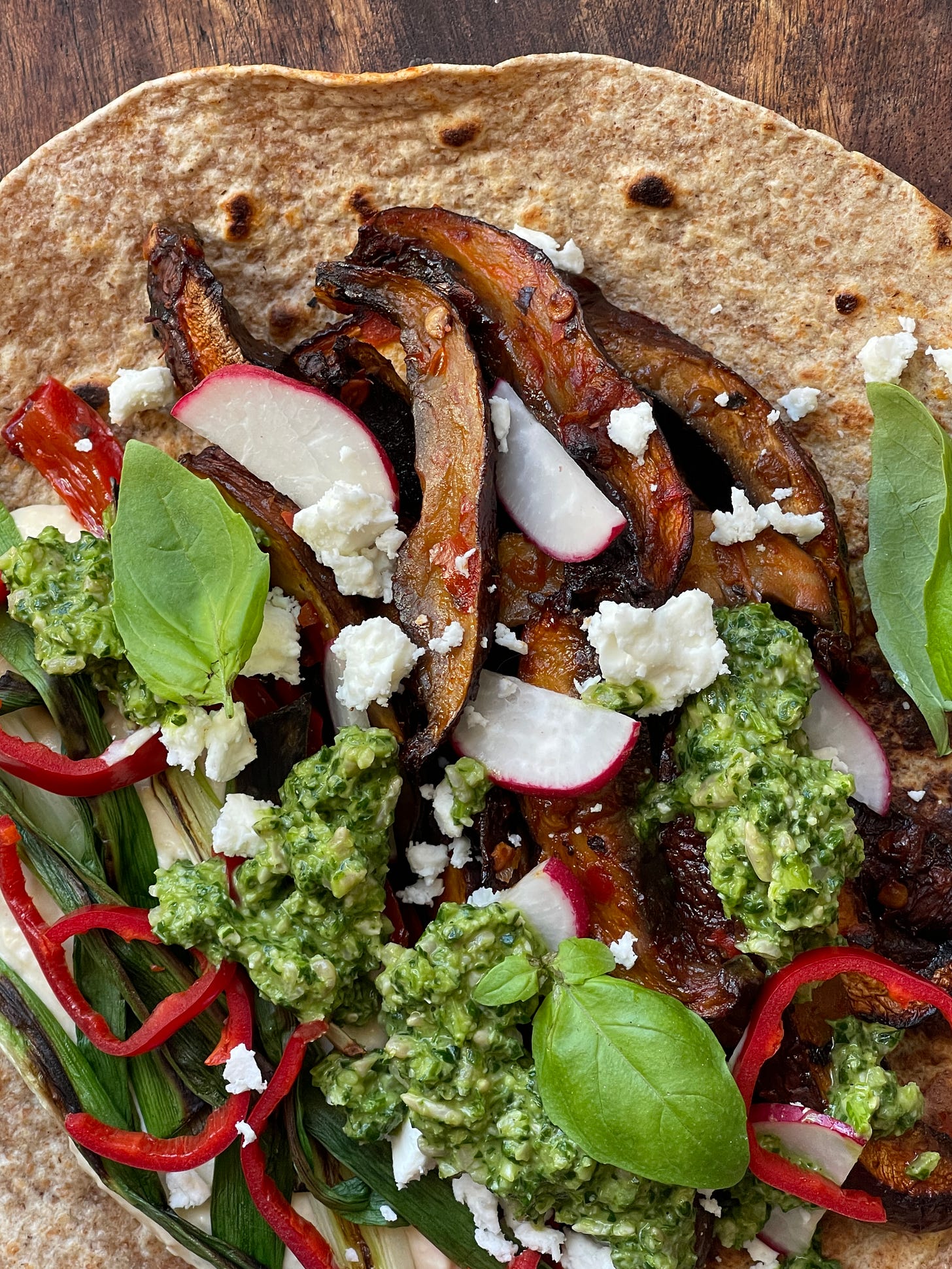 Detail of a plant-based mushroom shawarma flatbread with vibrant green pistachio pesto, charred scallions, and crumbled feta cheese