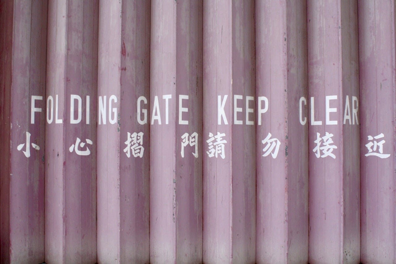 A folding metal gate in Hong Kong with the words 'Folding Gate Keep Clear' painted in English and Chinese. A folding metal gate in Hong Kong with the words 'Folding Gate Keep Clear' painted in English and Chinese.