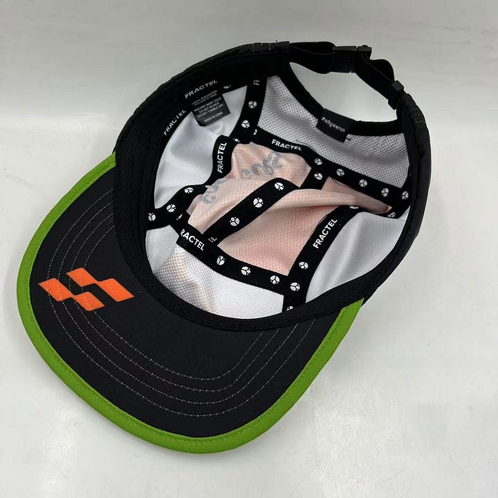 Images of the Footnotes Fractel hat including the orange logo on the front panel and underneath the brim. The newsletter's name is typed on the top of the hat and a green stripe accents the brim.