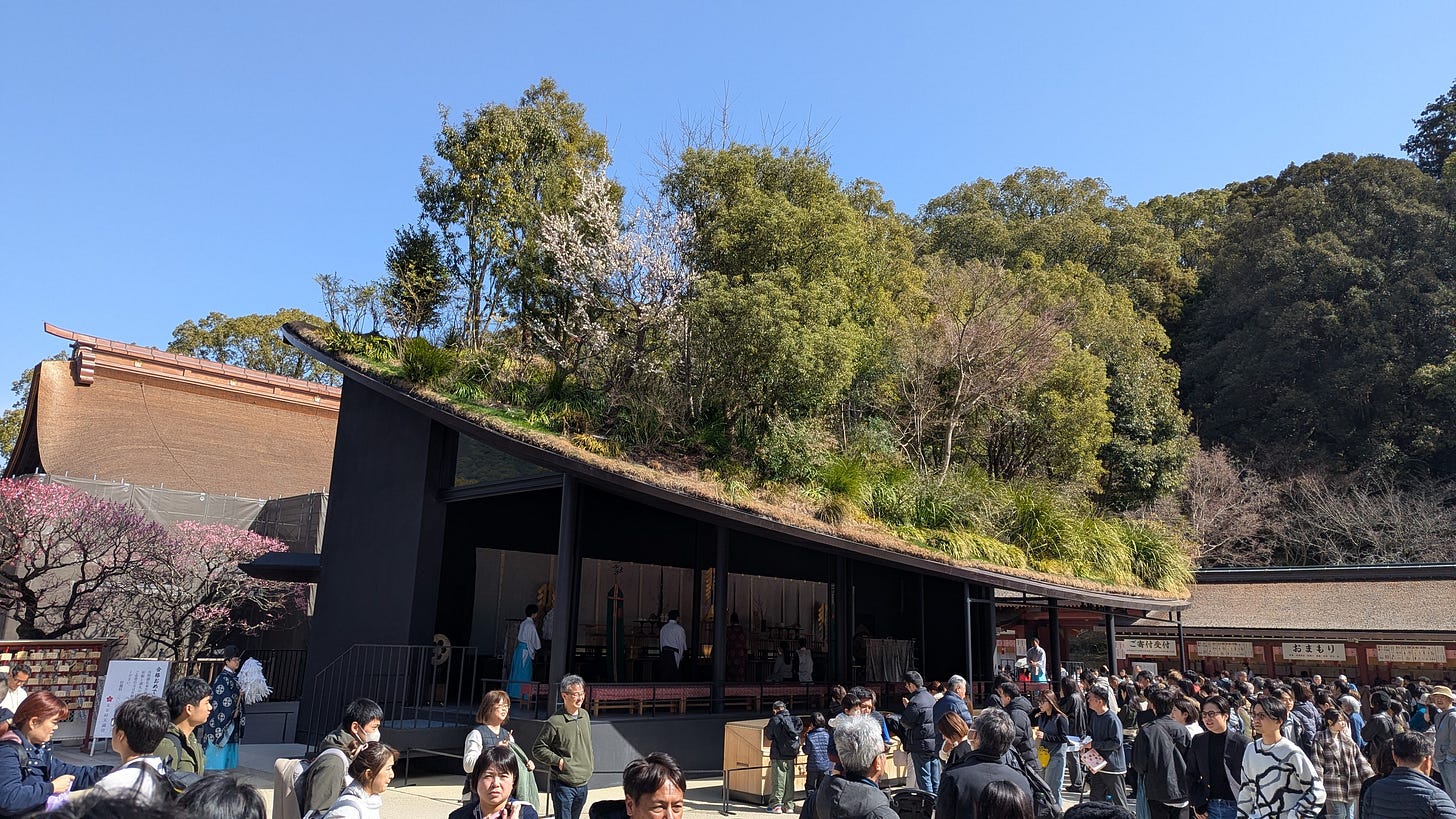 A crowd of people wait to pray at a shrine with trees on the roof.