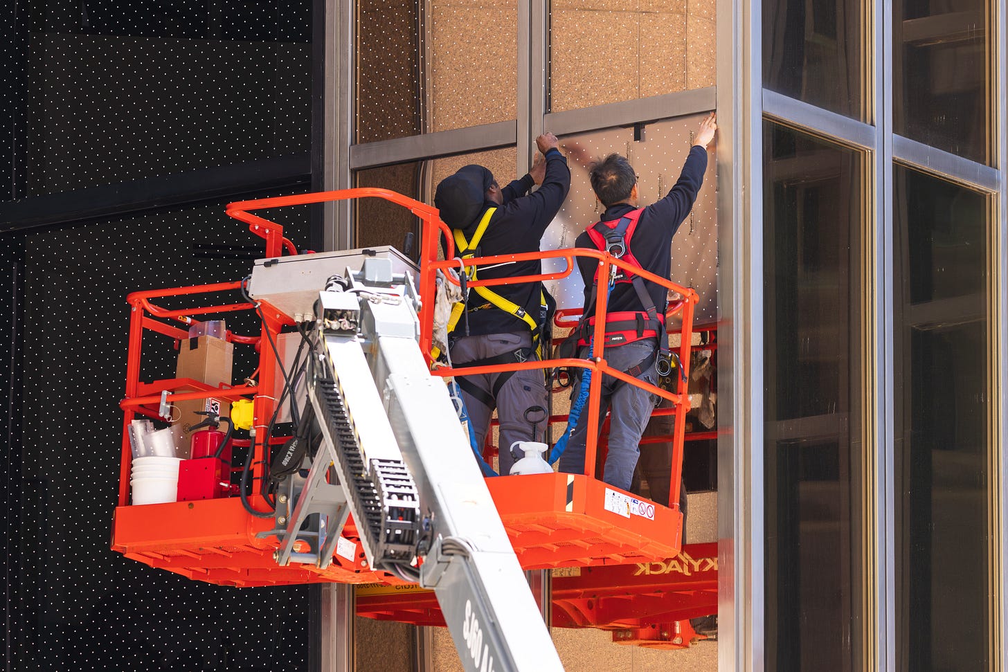 Two men on a boom lift install dotted window film on a glass facade.