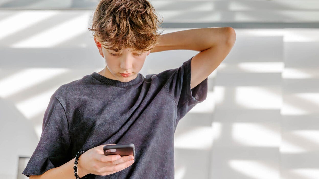 A teen boy looks down at his phone. A teen boy looks down at his phone.