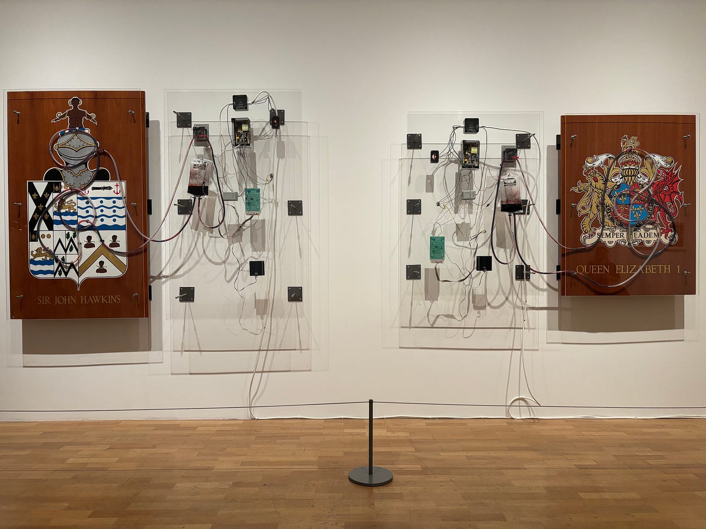 Visceral Canker (1990) by Donald Rodney. Installation view at Whitechapel Gallery, London. A simulation of a blood exchange system atop the wood-mounted heraldic crests of Queen Elizabeth I and Sir John Hawkins: architects of British empire