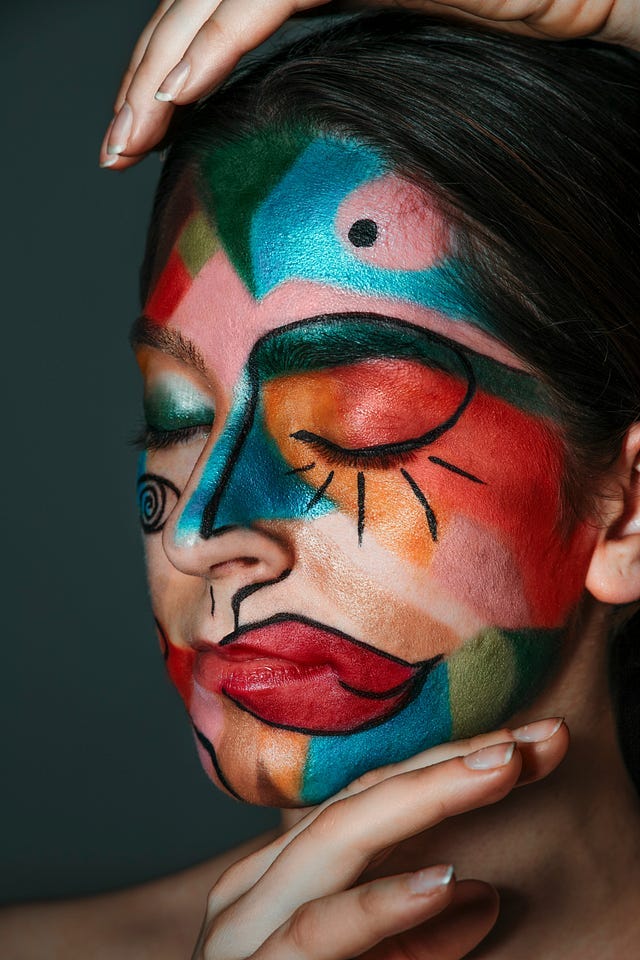 Close-up of a person’s face painted in vibrant, abstract patterns with bold colors, including red, blue, green, and orange, symbolizing creativity, complexity, and mental health. The person has their eyes closed and hands gently touching their face, evoking a sense of introspection and calm.