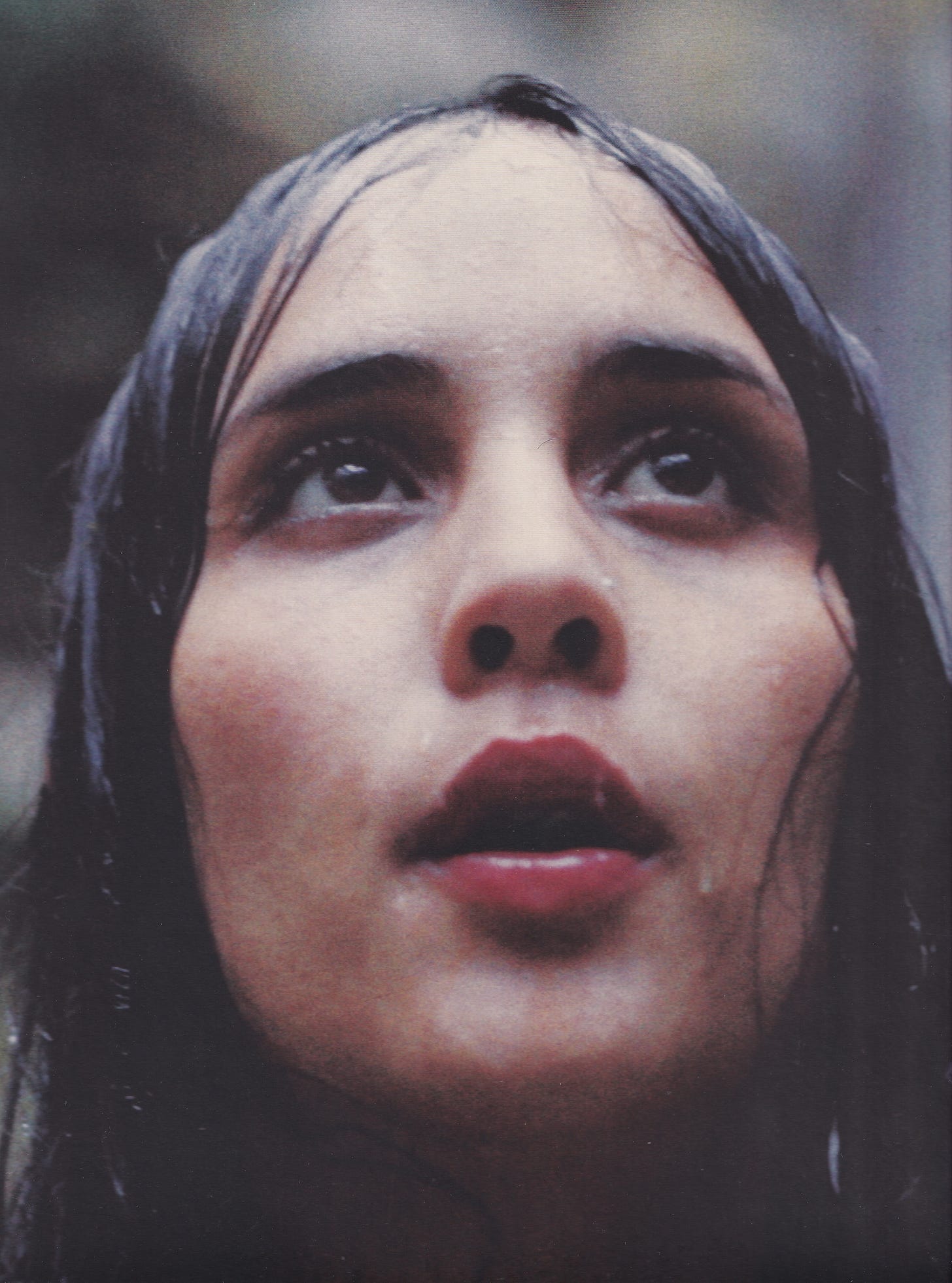 a scan of Melati Malay on the cover of Still Life by Young Magic. she stares at something in the distance while standing in front of a waterfall, her hair soaked and water dripping down her face.