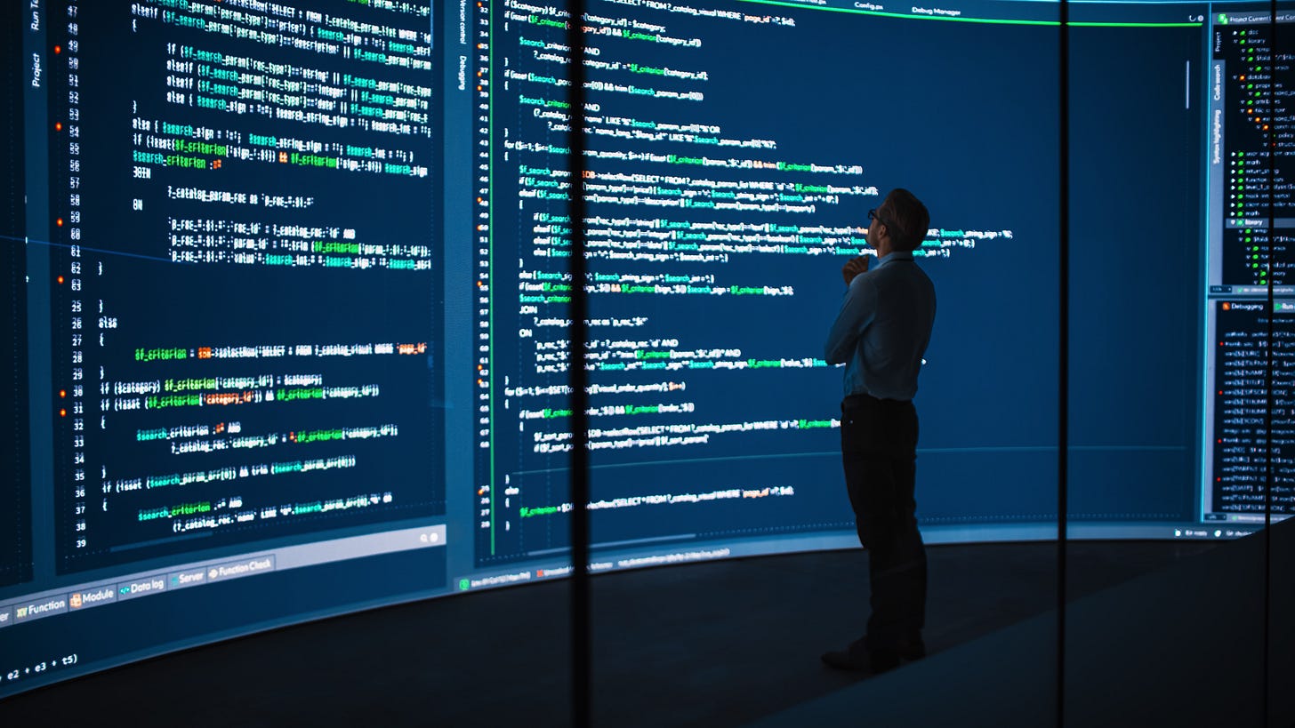 In a dark room, a silhouette of a man illuminated by a wall of computer code with green and white letters on a dark background. In a dark room, a silhouette of a man illuminated by a wall of computer code with green and white letters on a dark background.