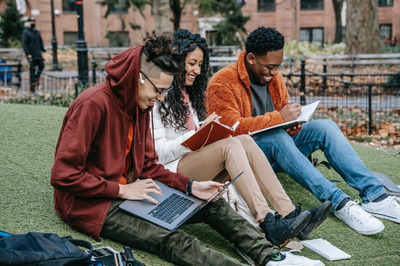 Three students laughing on a university campus lawn Three students laughing on a university campus lawn