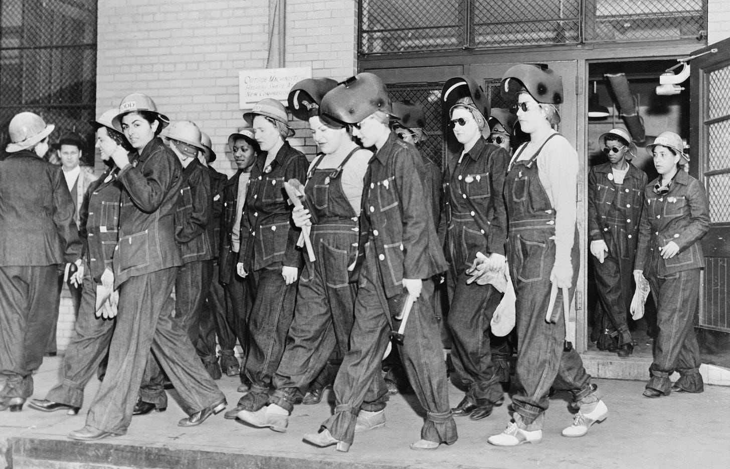 Women welders walk away from a door and wear denim overalls and helmets