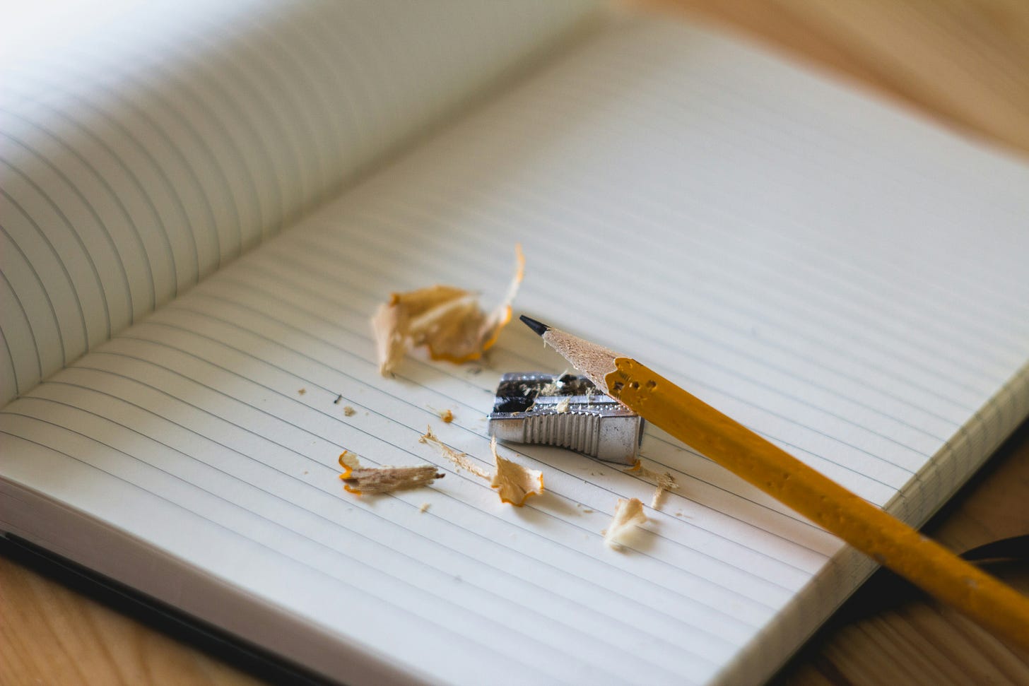 Image of a pencil, pencil sharpener, and pencil shavings atop a lined notebook