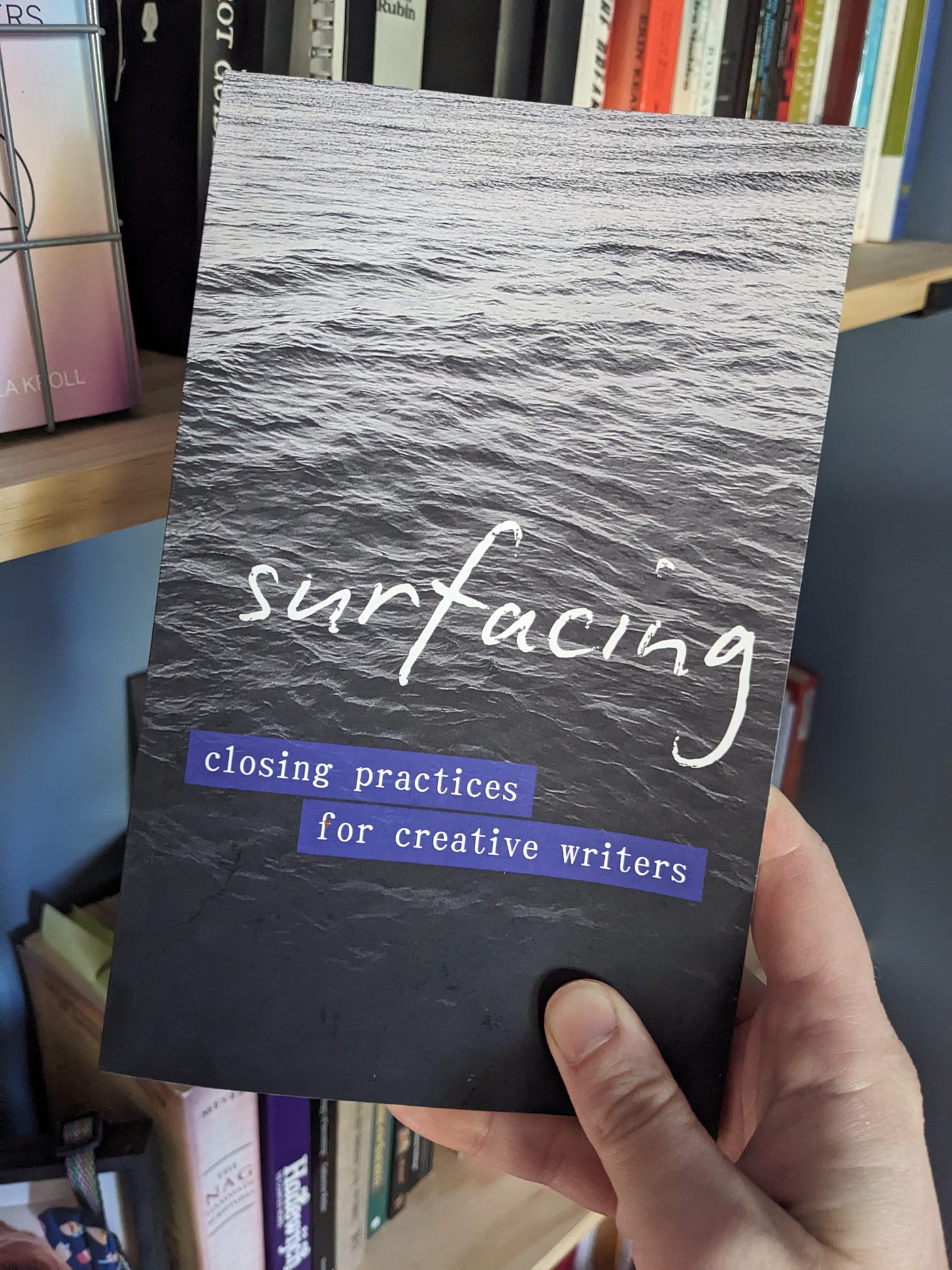 the front cover of a small book titled: Surfacing. The subtitle is white text on a purple background that reads: closing practices for creative writers. The photo background is an image of the waters of Lake Michigan in different shades of blue-black.