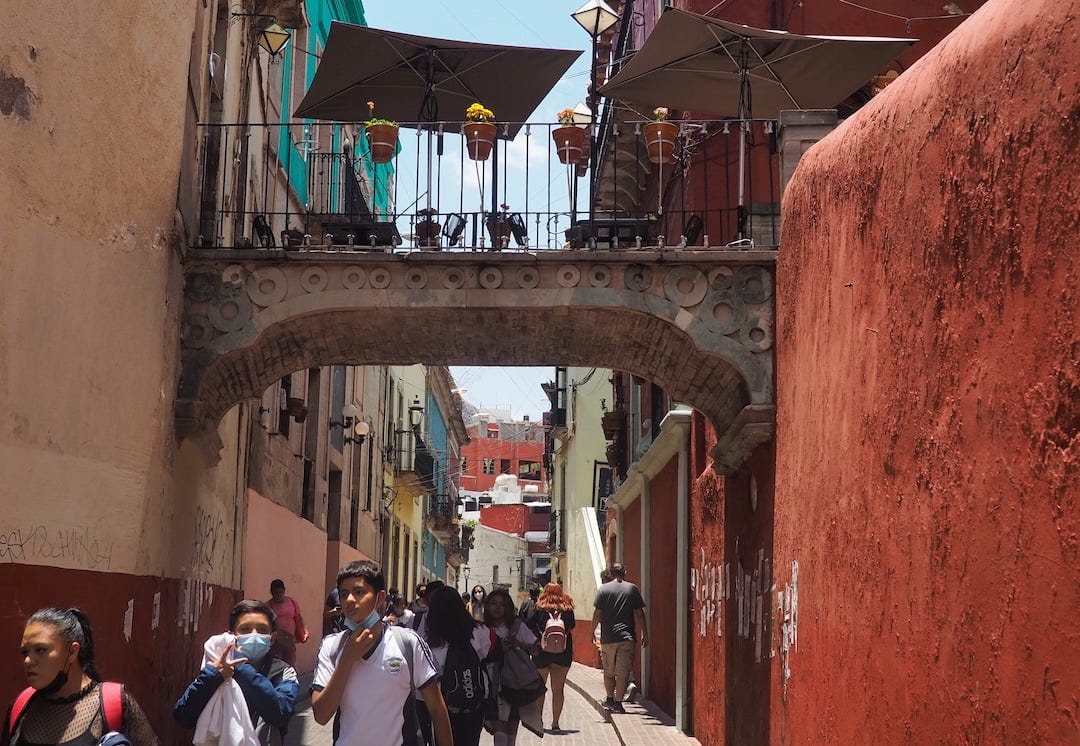 A bridge crosses a narrow pedestrianised street with a couple of tables and chairs on top