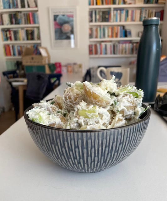 best potato salad ever in a fancy bowl on a white counter top with bookshelves and household mess in the background