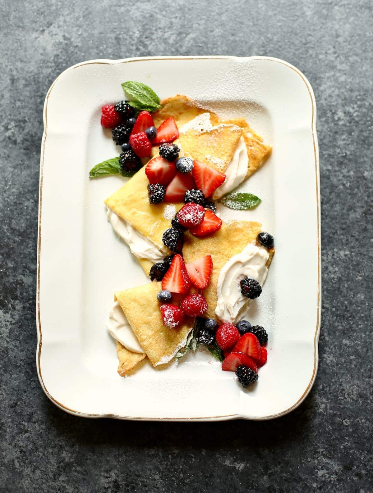 a gray table and a serving dish with crepes on it.