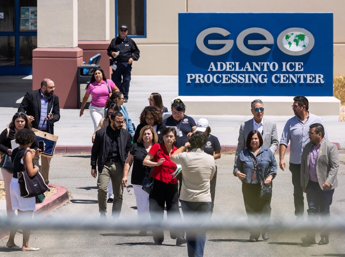 People leaving a building with a sign that reads 'GEO Adelanto ICE Processing Center'