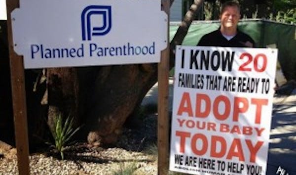 Un hombre está de pie junto a un cartel de Planned Parenthood. Sostiene un cartel que dice: "Conozco a 20 familias que están dispuestas a adoptar a su bebé hoy mismo". Estamos aquí para ayudarte". Pie de foto: "Hay aproximadamente 36 parejas que esperan adoptar por cada bebé disponible en Estados Unidos. Esto lleva a actos desesperados".