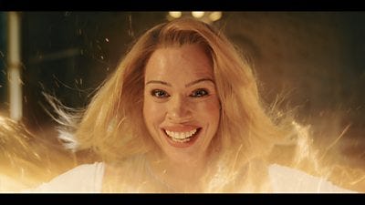 A woman with blonde hair smiles as her face emerges through regeneration energy