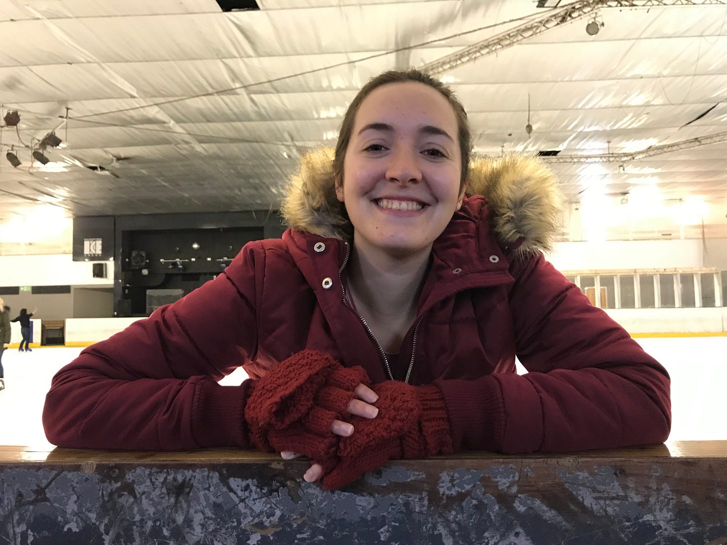 Holly in a red coat and gloves leaning on the edge of an ice rink Holly in a red coat and gloves leaning on the edge of an ice rink