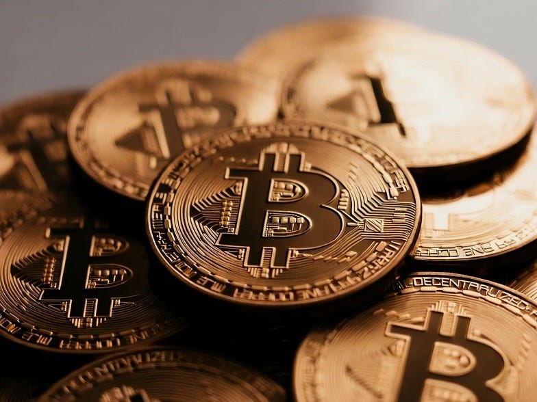 A photograph of stacked Bitcoin coins in a blurred indoor setting, emphasizing their physicality.