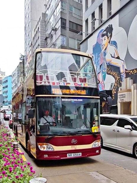 Double-decker bus on Hong Kong street with colorful mural, part of Big Bus Tour.
