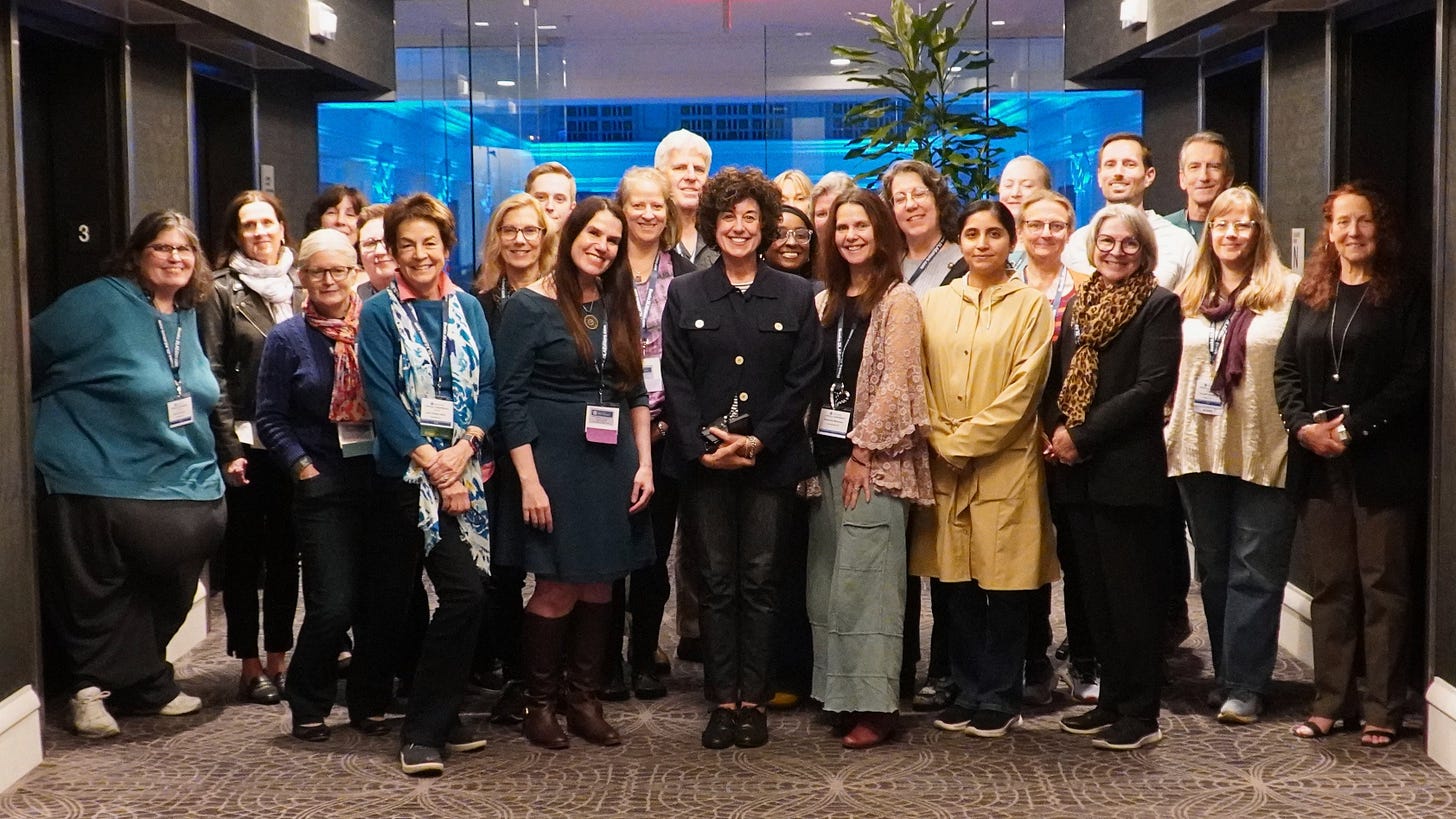 About two dozen people stand together in a hotel hallway. They smile at the camera wearing lanyards for the Writer’s Digest Conference. At the center stands writer Ann Garvin. 